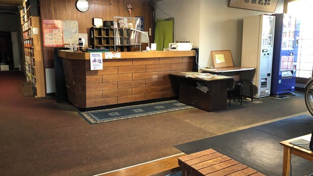 A reception desk with a wooden counter, a computer, and a vending machine. - Shoraku Ryokan (Ozu)