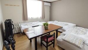 A room with a wooden table, a red chair, and two beds with white bedding. - Traveler's Inn Takagi (Matsumoto)