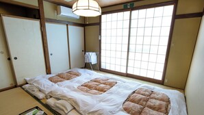 A traditional Japanese room with tatami flooring, a futon bed, a washboard, and a sliding door. - Traveler's Inn Takagi (Matsumoto)