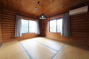 Una habitación con paredes de madera, esteras de tatami, dos ventanas con cortinas y un equipo de aire acondicionado.