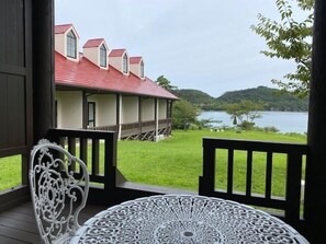 Un espacio al aire libre cubierto con una mesa y sillas, con vista a un lago y un edificio con tejados rojos.