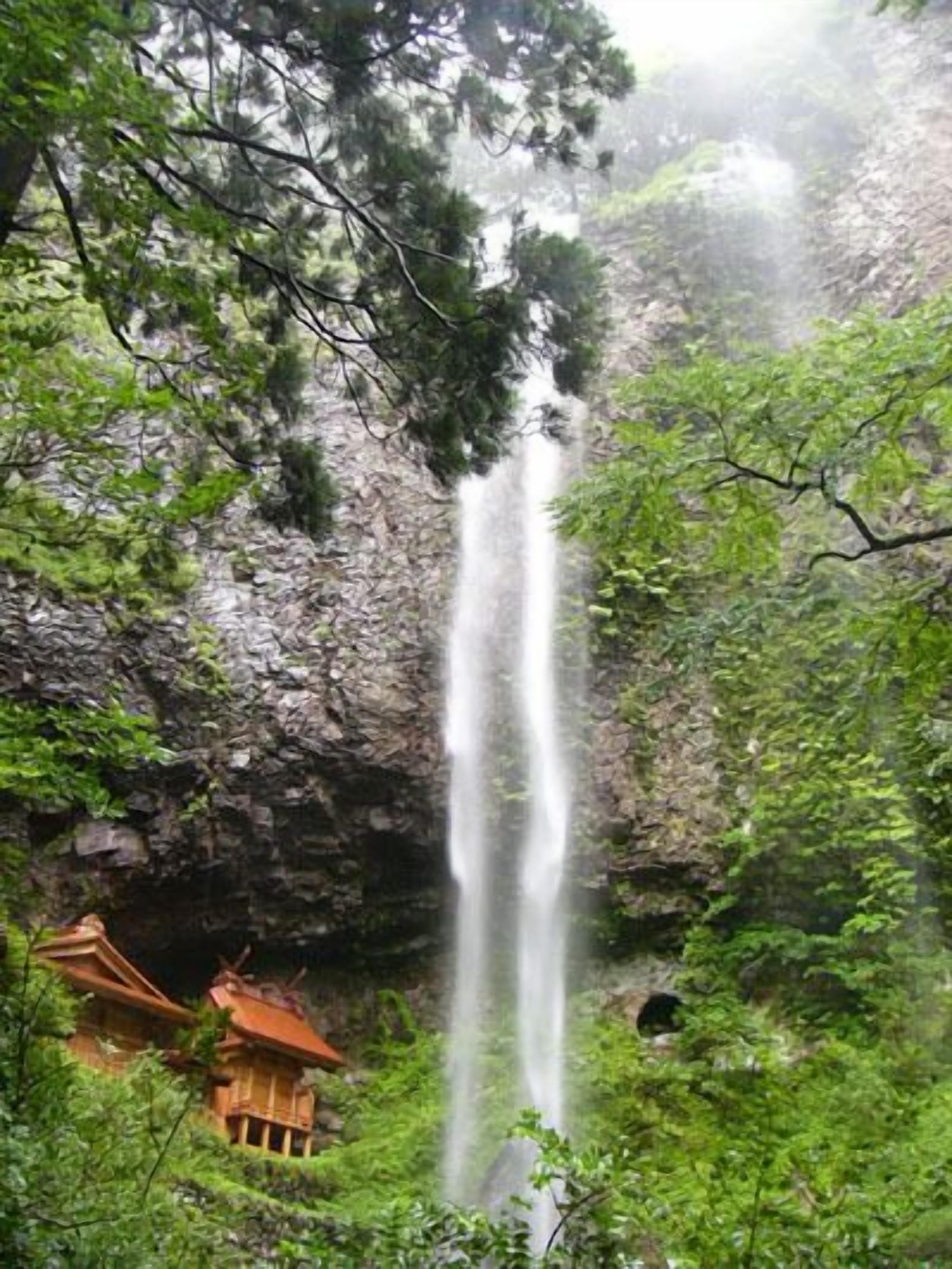 A waterfall surrounded by lush greenery and a traditional building.