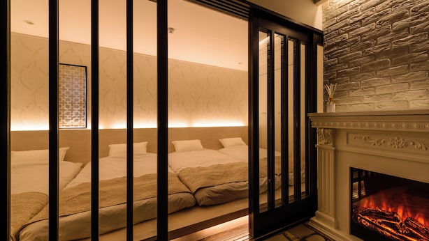 A bedroom with a bed, a fireplace, and a stone wall. - Guest Villa Hakone Yumoto (Hakone)