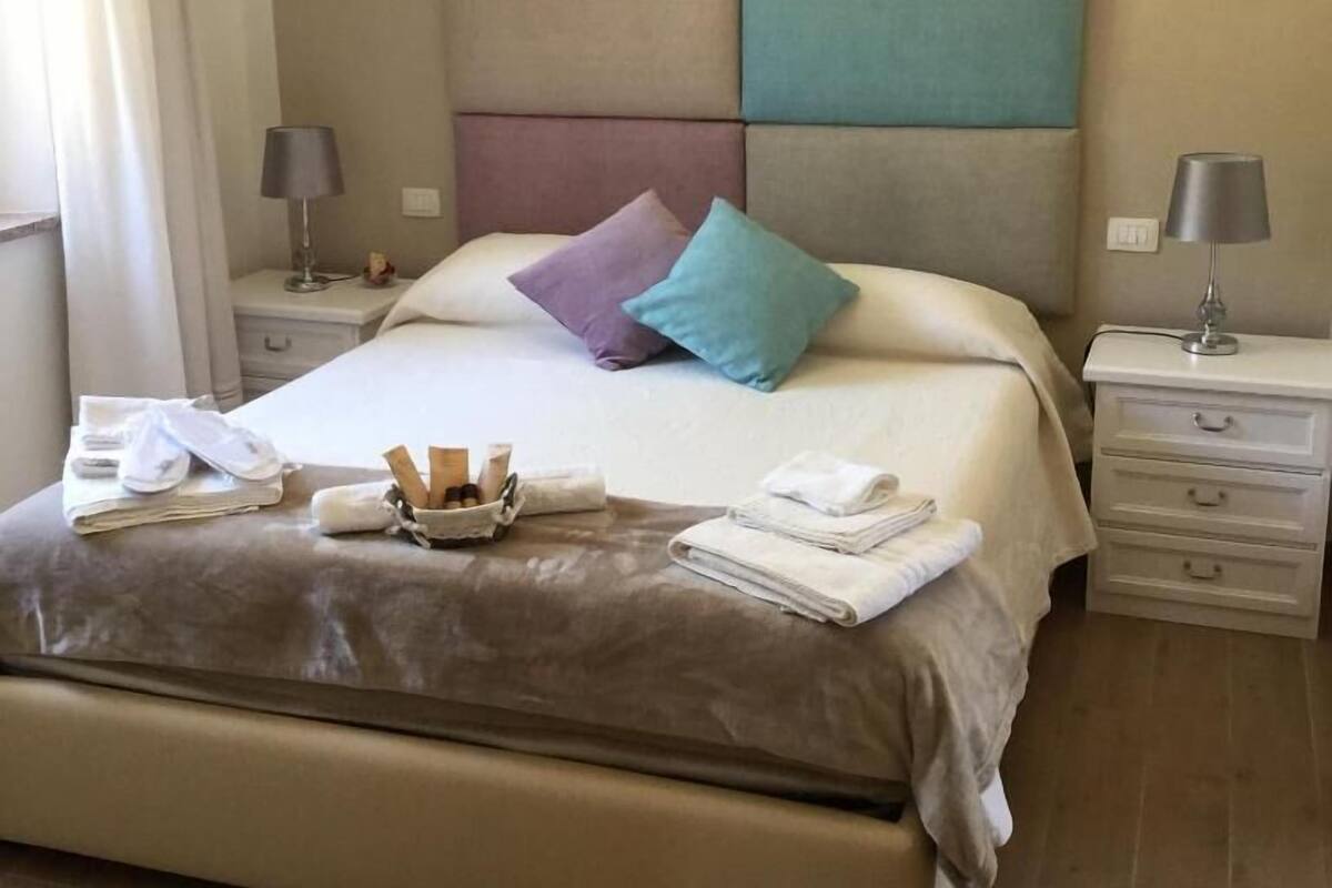 A neatly made bed with pillows, a bedside table with a lamp, and a small tray with toiletries.