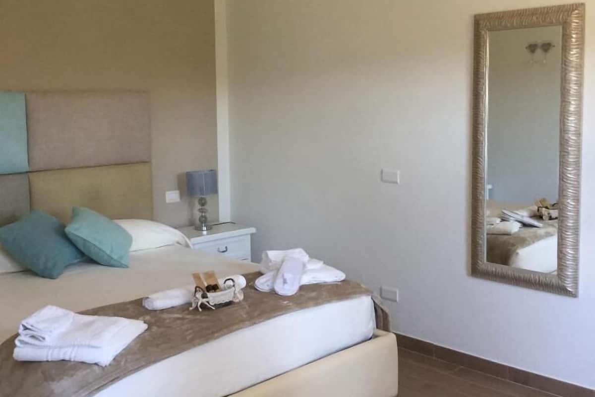A hotel room with a bed, bedside table, lamp, and a large mirror.