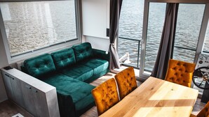 A modern room with a green sofa, wooden dining table, and a view of the water.