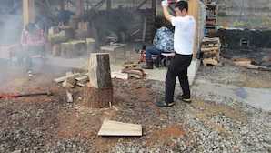 A man using a hammer to break wood in an outdoor setting with a wooden structure in the background. - Guest House Amigo (Toyooka)