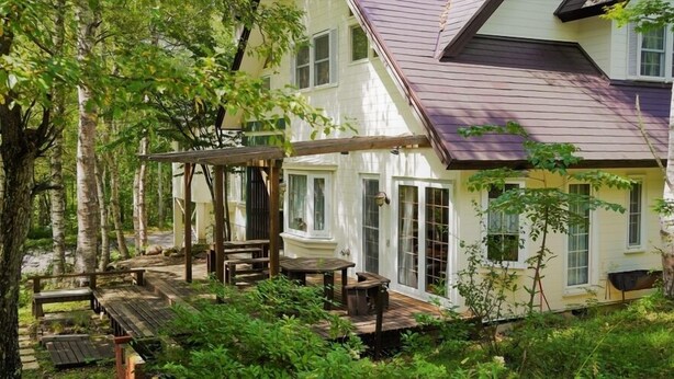 A two-story house with a covered patio area, a wooden deck, and a garden. - Winds (Tateshina)