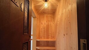 A wooden interior with a sloped ceiling and a light fixture. There are wooden shelves and a door with a vent. - Winds (Tateshina)