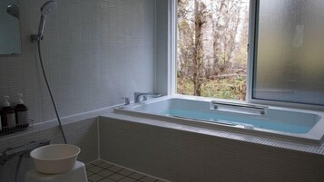 Un baño moderno con una bañera grande, una ventana con vistas a árboles y un cabezal de ducha.
