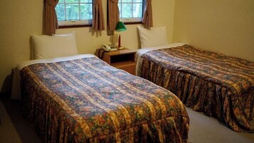 Una habitación con dos camas individuales, una mesita de noche con lámpara y una ventana con cortinas.