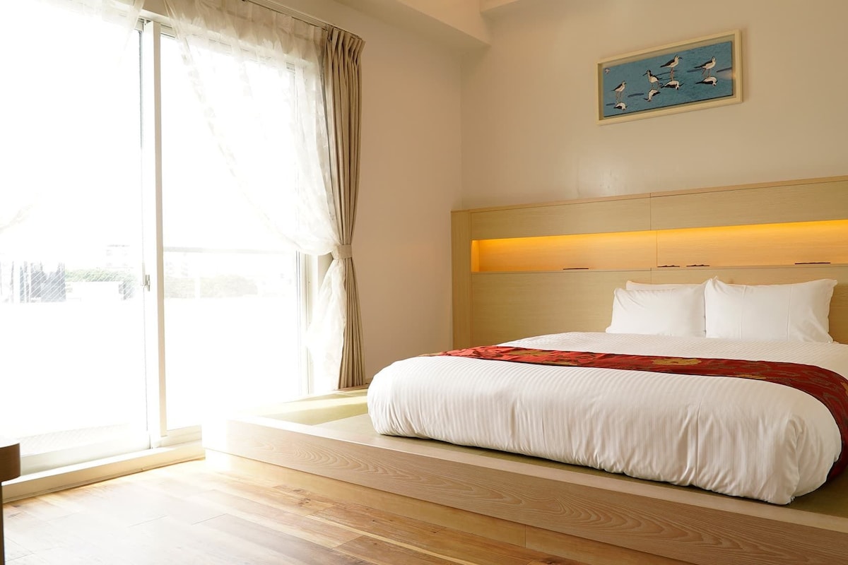 Habitación de hotel con una cama grande, cabecera de madera, un cuadro en la pared y vistas a través de la ventana.