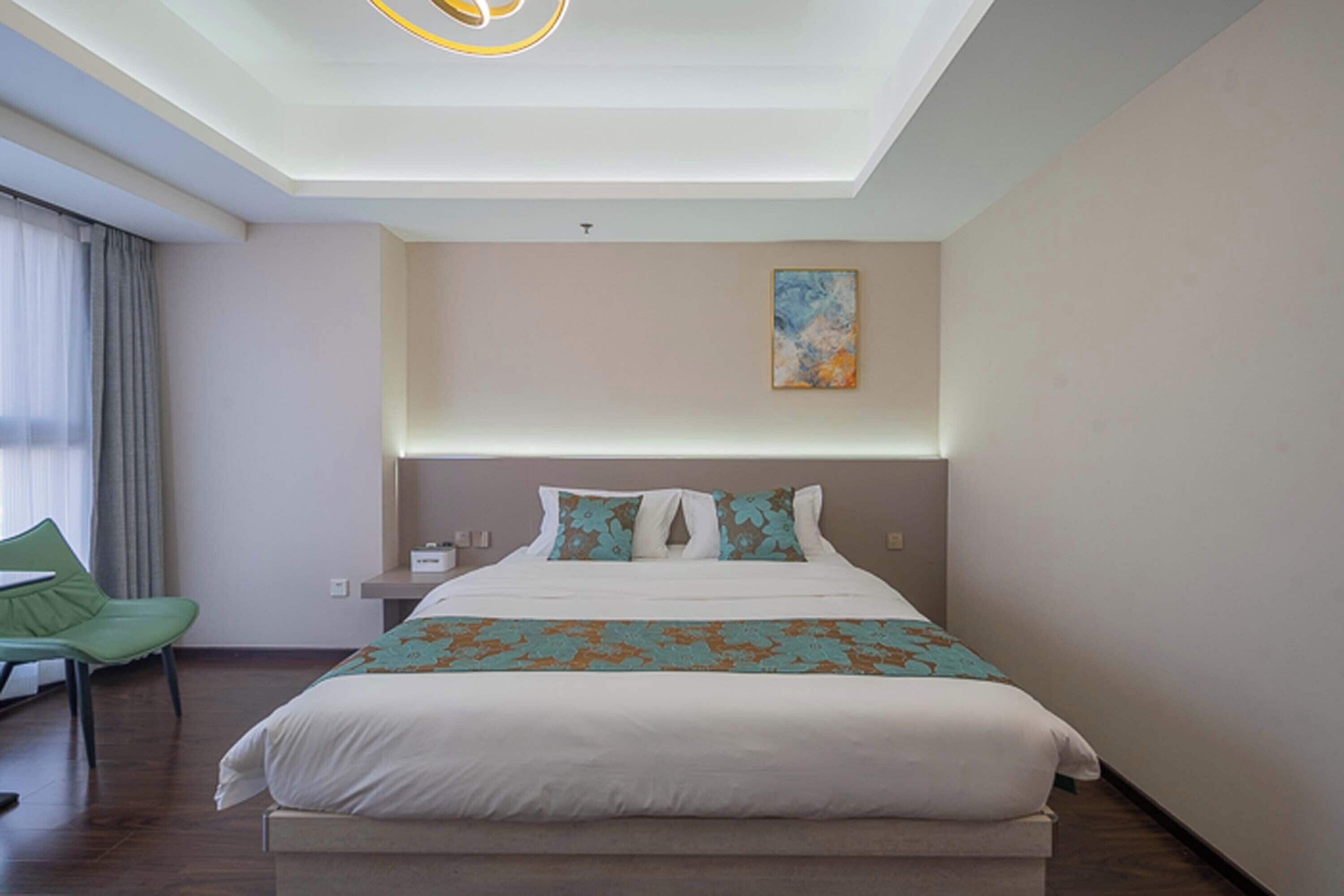 A modern hotel room with a large bed, a green chair, and a ceiling light fixture.
