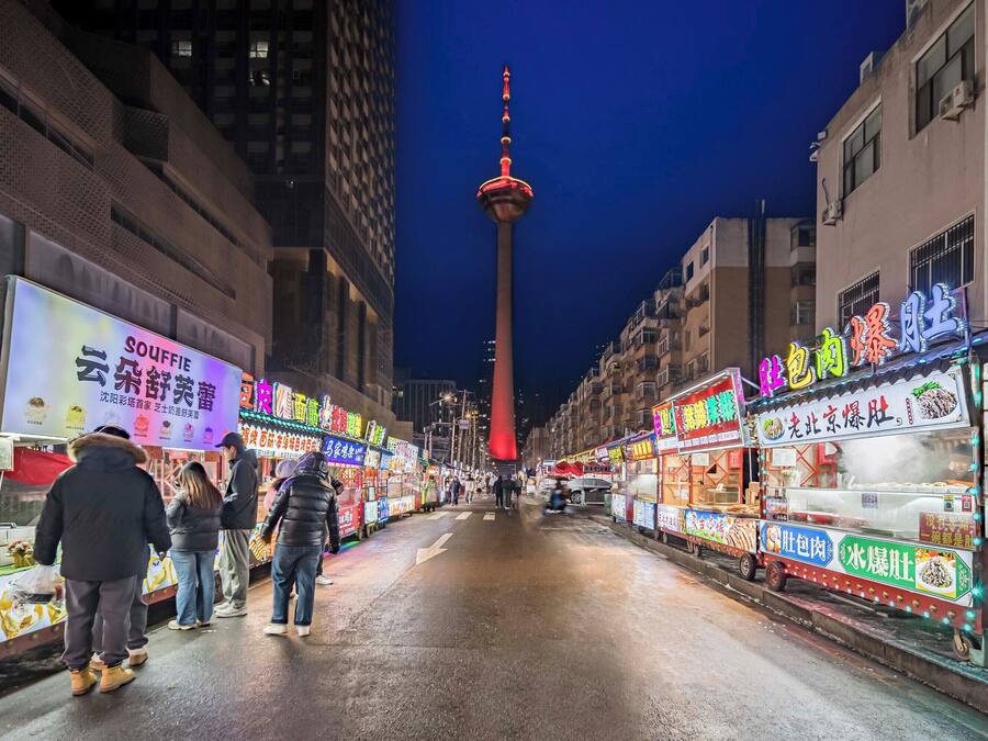 Una calle llena de puestos de comida iluminados intensamente por la noche.