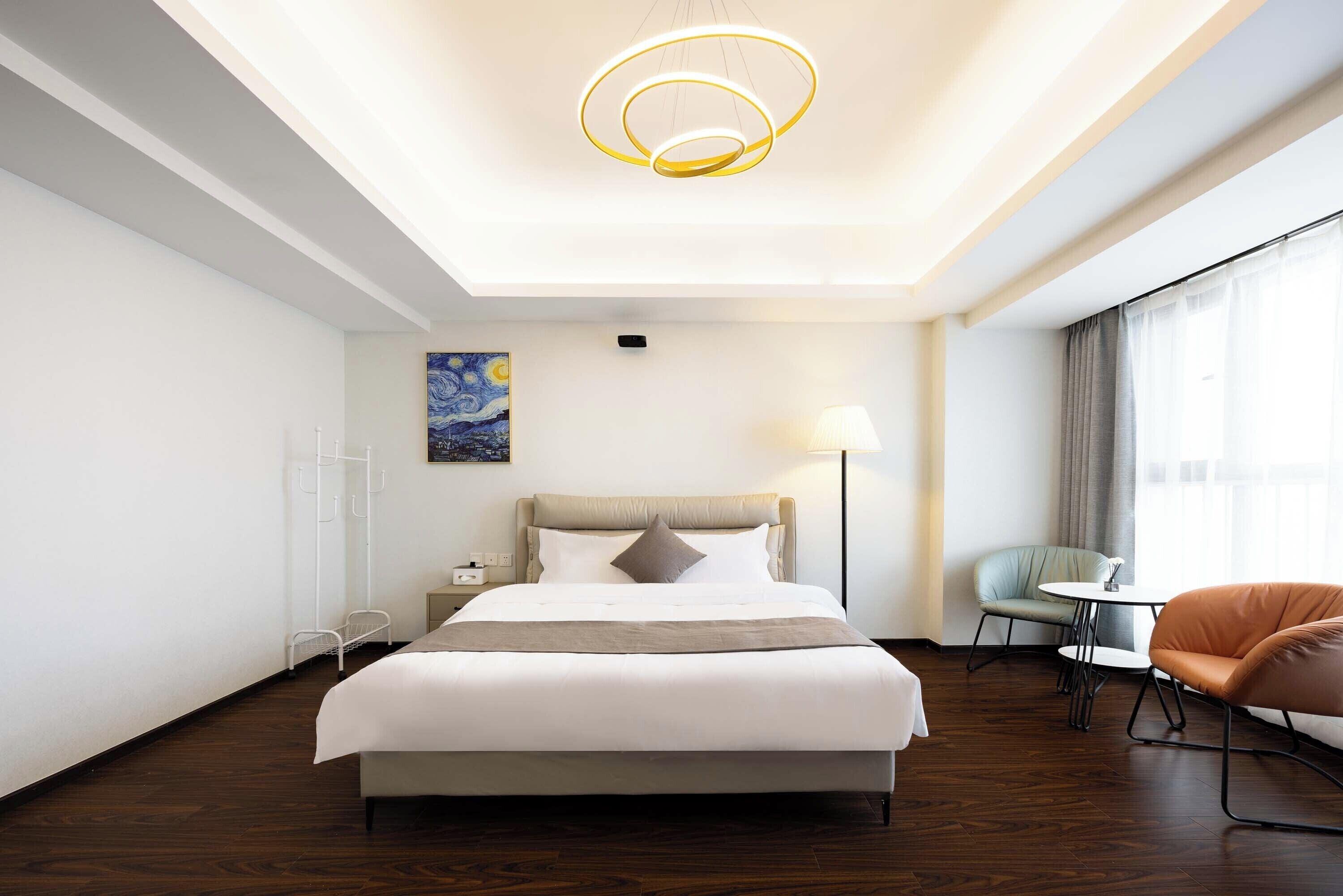 A modern hotel room with a large bed, a bedside table, a lamp, a chair, and a small table.
