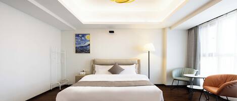 A modern hotel room with a large bed, a bedside table, a lamp, a chair, and a small table.
