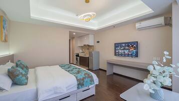 A modern hotel room with a bed, a desk, a small kitchenette, and a ceiling light fixture.