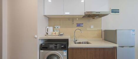 A compact kitchen with a washing machine, a coffee maker, and a refrigerator.