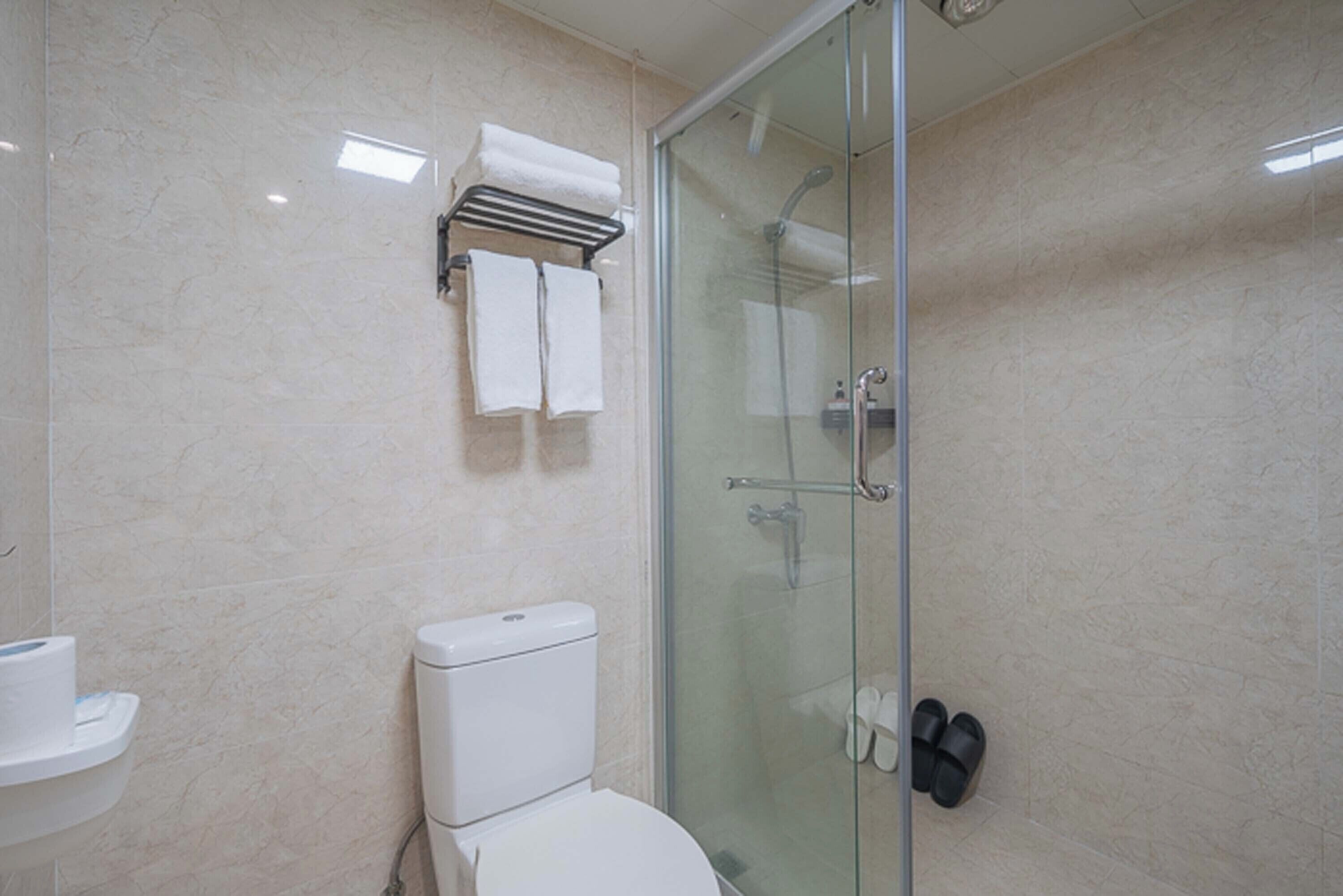 Un baño moderno con ducha de vidrio, inodoro y toquilla con dos toallas blancas.