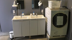 A bathroom with a double sink, a mirror, a hairdryer, a washing machine, and a trash bin. - Hostel und Kitchen Goto Base <goto, Nakadorijima> (Shinkamigoto)