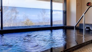 Un manantial de agua termal con vistas a árboles y montañas a través de amplios ventanales.