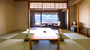 Una habitación japonesa tradicional con suelo de tatami, una mesa baja y un puertas correderas que dan a un balcón con sillas.