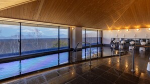 Una piscina interior moderna con amplios ventanales, suelo húmedo y zona de sauna.