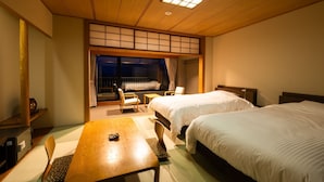 Habitación de hotel con dos camas, una mesa de madera y vistas al exterior a través de una puerta corrediza.