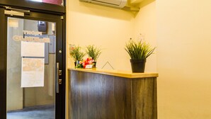 A reception desk with a wooden counter, potted plants, and a wall-mounted air conditioner. - Mr.kinjo in Arcade Ange Miona (Naha)