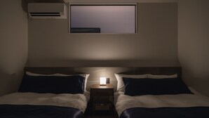 Una habitación pequeña y con poca luz, con dos camas, una mesita de noche, una ventana y un equipo de aire acondicionado.