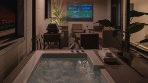 Un baño moderno con una bañera grande, una pantalla de televisión mostrando un partido de béisbol y mobiliario de mimbre.