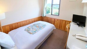 A single bed with a patterned bedspread, a bedside table with a lamp, a television, and a telephone. - Business Hotel New Daiei (Ashikaga)