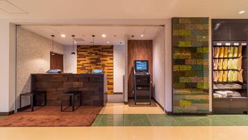 A reception area with a wooden reception desk, a digital kiosk, and a wall with a green and brown patterned design.