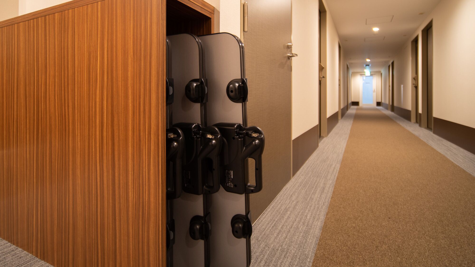 A hotel hallway with a wooden panel wall, a luggage trolley, and a carpeted floor.