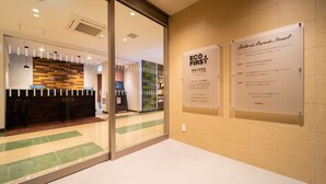 Un espace d’accueil d’hôtel doté d’une cloison en verre, d’un comptoir de réception et d’un panneau mural indiquant les différentes initiatives écologiques mises en place par l’hôtel.