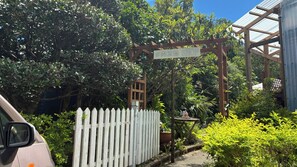 Une pergola en bois, sur laquelle on peut lire l’inscription « Boucherie », se trouve dans un jardin agrémenté d’une clôture blanche et d’une végétation luxuriante.