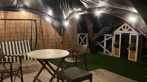 An outdoor patio area with a round table and chairs, a striped sofa, and a small building with a white door. - K's Fun Garden Inn Nakijin (Nakijin)