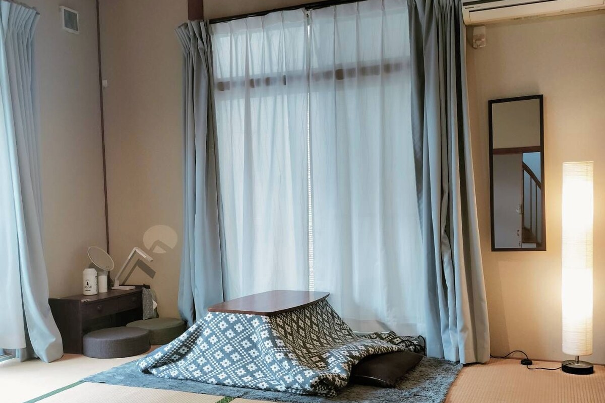 A traditional Japanese-style room with tatami flooring, a low wooden bed, a small bedside table with a mirror, and a wall-mounted air conditioning unit.