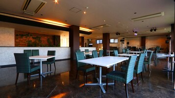 Un restaurante espacioso con mesas y sillas altas, un escenario con instrumentos musicales y una pared decorada con plantas.