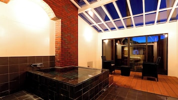 Un baño moderno con ducha envuelta en vidrio, pared decorada con ladrillos y vista a un dormitorio a través de una puerta de cristal.