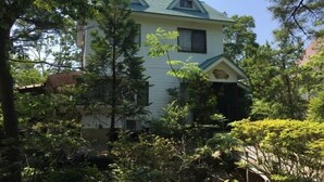 A two-story house with a gabled roof, surrounded by dense greenery. - Heartland Hills in Noto 5 Ike no Hotori House (Shika)