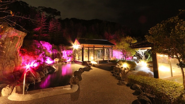 Un jardin japonais traditionnel, illuminé la nuit, avec des allées éclairées, un étang et un petit pavillon.