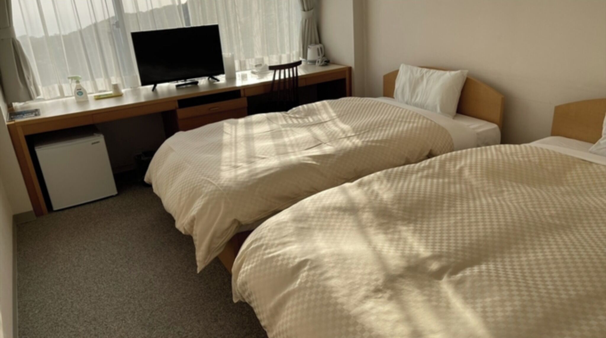 Une chambre d’hôtel avec deux lits, un bureau avec un ordinateur et un petit réfrigérateur.