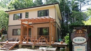 Een gebouw met twee verdiepingen, voorzien van een houten pergola, gelegen in een bebost gebied.