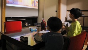 Two children playing with a toy car at a table with a projector screen displaying a cartoon. - Kinosaki Onsen Kinoie (Toyooka)