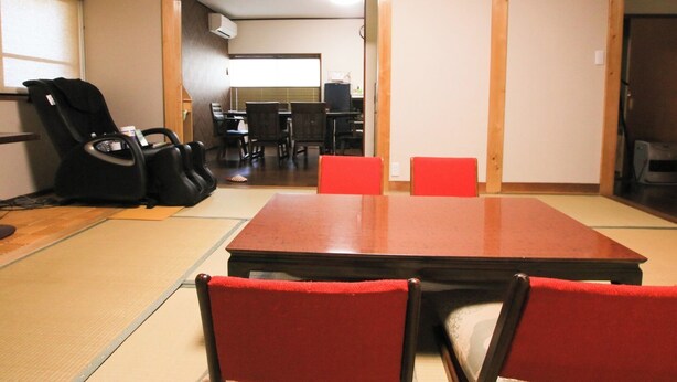 A tatami mat room with a low table, two red chairs, a black chair, and a projector mounted on the ceiling. - Kinosaki Onsen Kinoie (Toyooka)