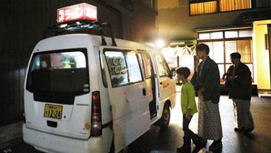 A white van parked at night with a red sign on top, a license plate, and a person standing next to it. - Kinosaki Onsen Kinoie (Toyooka)