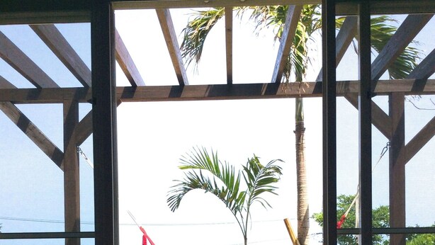 A wooden bench and a hammock in a covered outdoor area with a view of palm trees and a beach. - Somos (Nakijin)