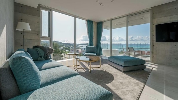 A modern living room with a large window, a sofa, a coffee table, and a TV mounted on the wall. - Okinawa Plaisant Villa (Onna)