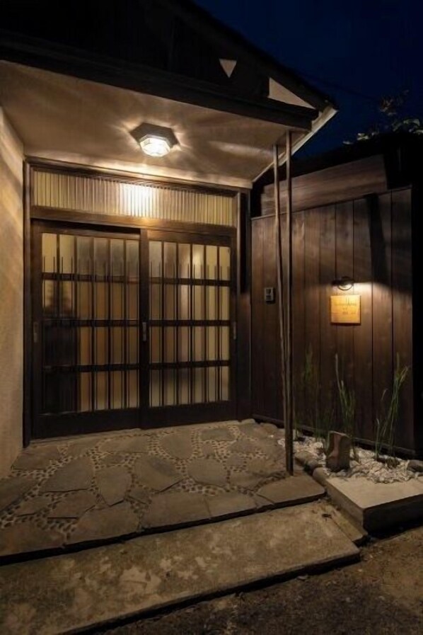Une porte en bois sombre, surmontée d’une enseigne lumineuse, qui mène à une entrée pavée de pierres.